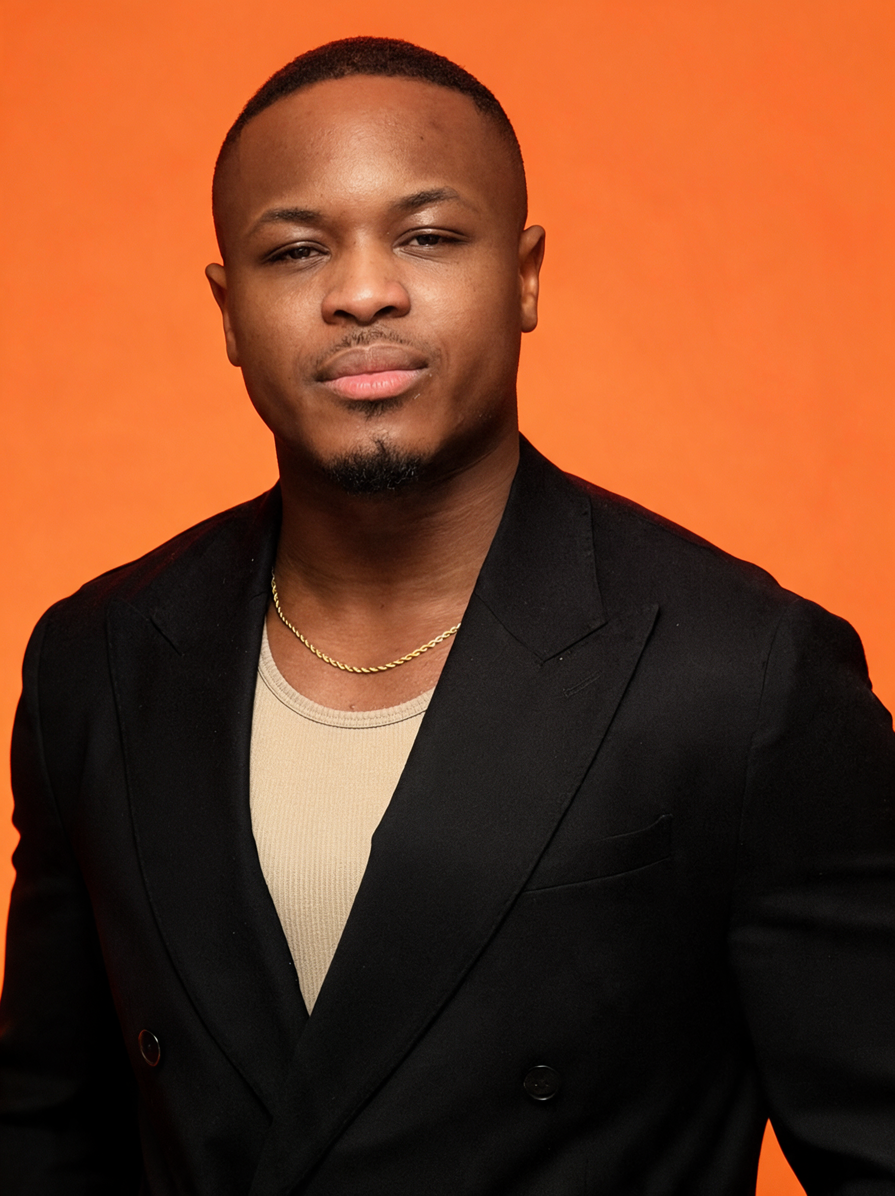 DeGraft, founder of Goldsmith Collective Trading, wearing a black blazer against an orange background